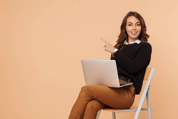 美しい驚くほど若い女性が分離ラップトップ コンピューターを指して使用して椅子に座っているポーズの画像 — ストック写真
