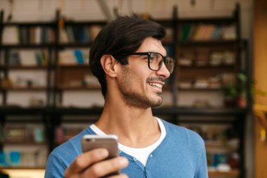 Cep telefonu kullaranarak kütüphanede, gözlük takan yakışıklı bir genç adam yakın çekim