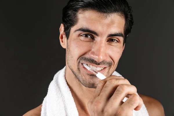一个英俊的年轻人的形象摆在黑暗的墙壁背景孤立刷牙他的牙齿 — 图库照片