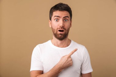 Şaşırmış bir genç adam portresi raslantı üzerinde bej, uzakta kopya alanı işaret izole ayakta giyinmiş