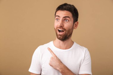 Şaşırmış bir genç adam portresi raslantı üzerinde bej, uzakta kopya alanı işaret izole ayakta giyinmiş