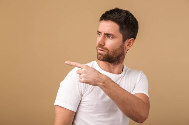 Üzgün bir genç adam portresi raslantı üzerinde bej, uzakta kopya alanı işaret izole ayakta giyinmiş