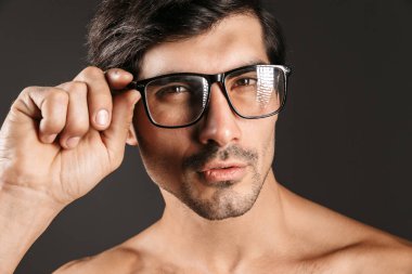 Gözlük takan koyu arka plan üzerinde izole ciddi konsantre yakışıklı bir genç adam görüntüsünü.