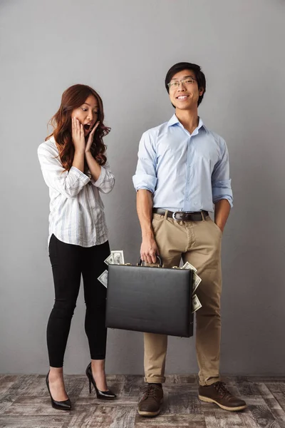 灰色の背景の上に立って お金紙幣のブリーフケースを持って興奮しているアジアのカップルの完全な長さ — ストック写真