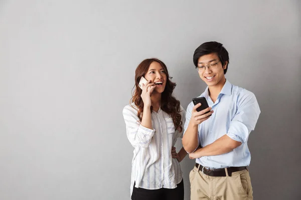 Feliz Pareja Asiática Pie Aislada Sobre Fondo Gris Utilizando Teléfonos —  Fotos de Stock