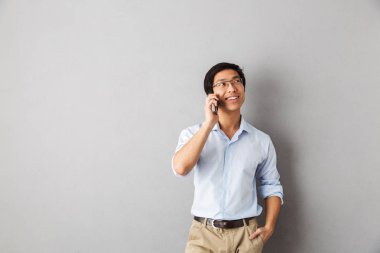 Cep telefonu üzerinde konuşurken gri arka plan üzerinde izole gülümseyen Asya iş adam ayakta