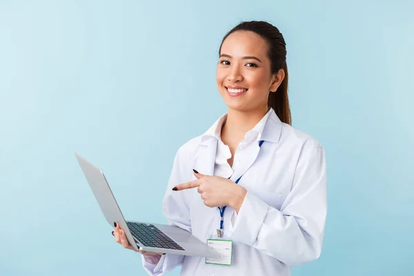 ラップトップ コンピューターを使用して青い壁背景に分離されたポーズの若い女性医師の写真 — ストック写真