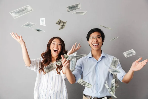 愉快的亚洲商务夫妇站在货币下钞票淋浴隔离在灰色背景 — 图库照片