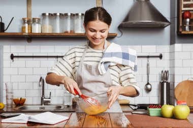 Mutlu genç kadın evde mutfakta ayakta, yumurta bir kase karıştırma
