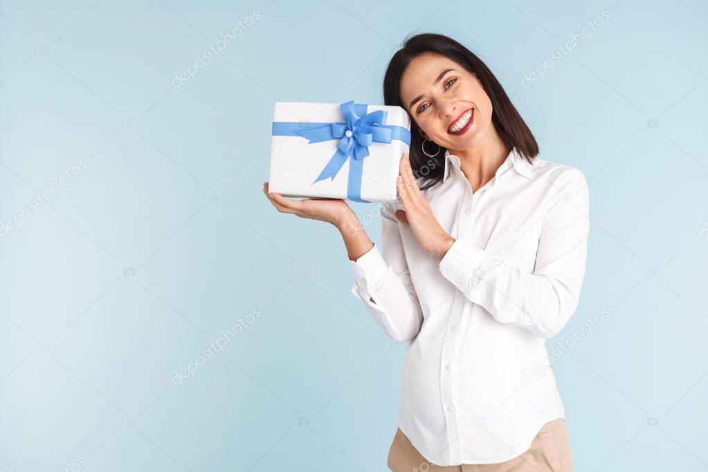 Image of a beautiful happy young pregnant business woman isolated over blue wall background holding gift box.