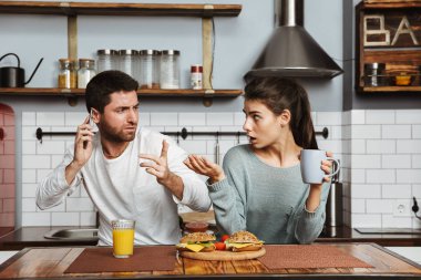 Cep telefonu tutan bir sorun mutfak evde, öğle yemeği sırasında oturan mutsuz genç çift