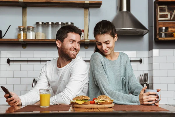 Feliz Pareja Joven Sentada Cocina Durante Desayuno Casa Utilizando Teléfono — Foto de Stock