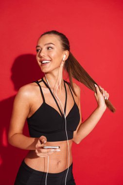 Genç sporcumuz kırmızı arka plan üzerinde duran cep telefonu tutan kulaklık ile müzik dinlemek güzel bir portresi uygun