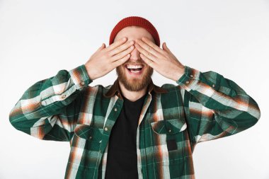 Şapka ve beyaz arka plan üzerinde izole ayakta iken avuç içi ile yüzünü kaplayan ekose gömlek giyen gülümseyen adam portresi