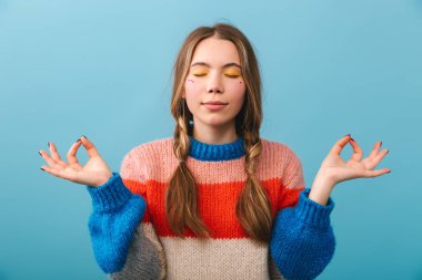 Üzerinde mavi arka plan, izole kazak ayakta giyen neşeli kız meditasyon