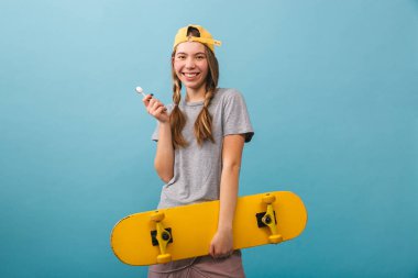 Kaykay holding neşeli şirin kız mavi arka plan üzerinde izole ayakta