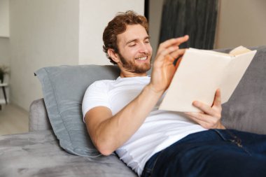 Yakışıklı bir genç sakallı adam evde kanepe görüntüsünü kitap okuma.