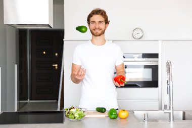 Yakışıklı bir genç adam evde mutfak at fotoğrafı sebze yemek yapmak salata.