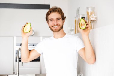 Mutfakta ev pişirme holding avokado, yakışıklı bir genç adam fotoğrafı.