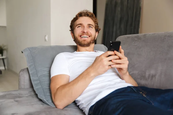 Imagen Guapo Joven Barbudo Sofá Casa Usando Teléfono Móvil — Foto de Stock