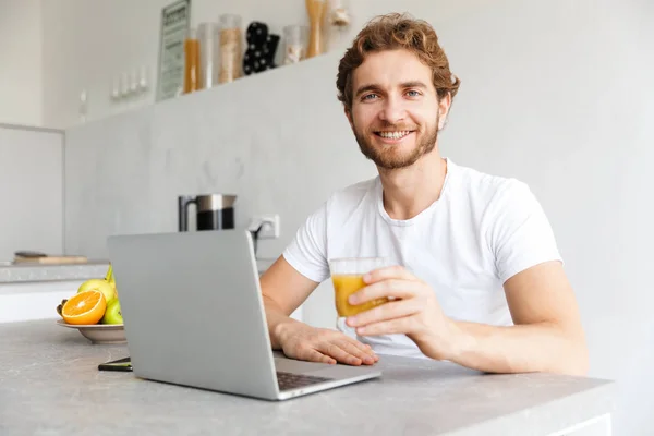 テーブルで幸せな若いひげを生やした男の写真は自宅のラップトップ コンピューターを使用してください — ストック写真