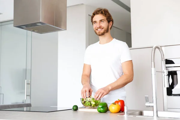自宅の台所でハンサムな若い男の写真料理野菜作るサラダ — ストック写真