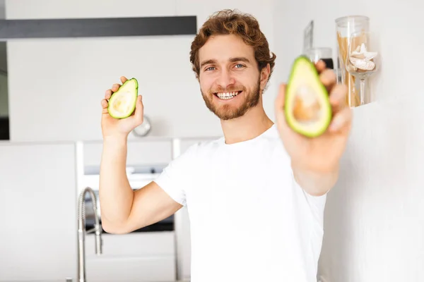 Foto Jovem Bonito Cozinha Casa Cozinhar Segurando Abacate — Fotografia de Stock