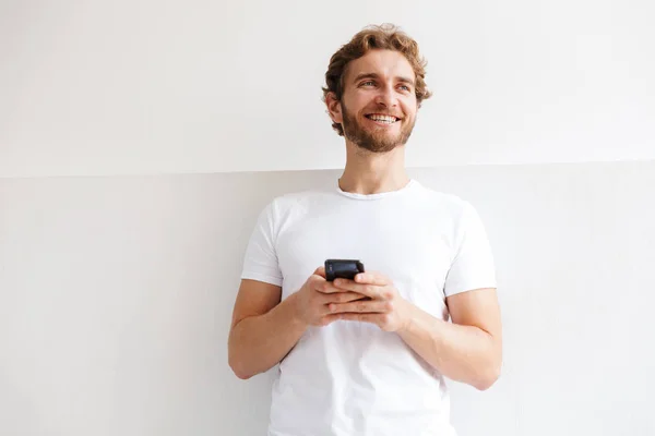 Leende Ung Man Håller Mobiltelefon Står Vid Väggen Hemma — Stockfoto