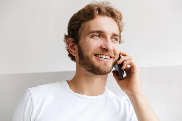 Smiling young man talking on mobile phone, standing at the wall at home