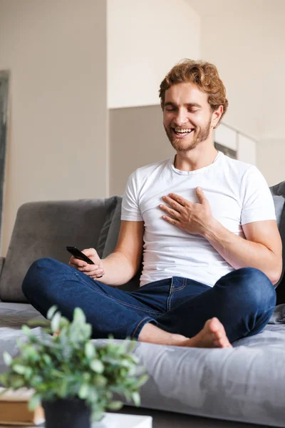 Foto Guapo Joven Feliz Sofá Casa Sosteniendo Control Remoto Ver —  Fotos de Stock