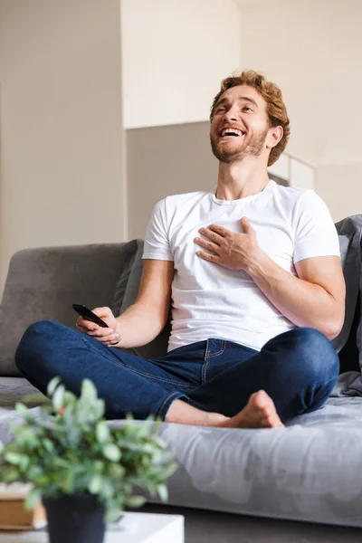 Foto Guapo Joven Feliz Sofá Casa Sosteniendo Control Remoto Ver — Foto de Stock