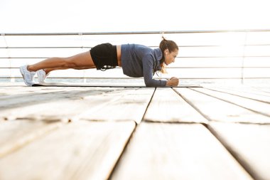 Plajda bir fitness mat tahta egzersizleri yapıyor sporcumuz konsantre