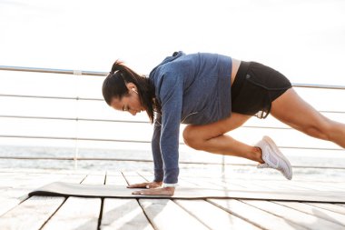 Plajda bir fitness mat tahta egzersizleri yapıyor konsantre bir sporcumuz yan görünüm