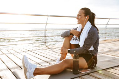 Bir güzel genç spor fitness kadın resim var bir dinlenme Sahilde açık havada kulaklık ile müzik dinleme.