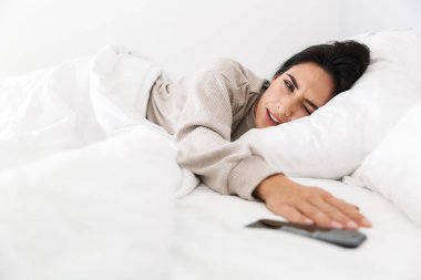 Fotoğraf memnun kadın 30'lu kapma baş beyaz keten evde yatakta yatarken smartphone nedeniyle