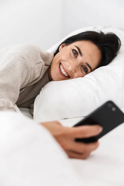 Zdjęcie Radosne Kobiety 30S Przy Użyciu Smartfona Podczas Leżenia Łóżku — Zdjęcie stockowe