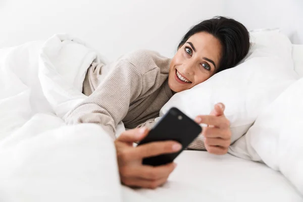Zdjęcie Wesoły Kobieta 30S Przy Użyciu Smartfona Podczas Leżenia Łóżku — Zdjęcie stockowe
