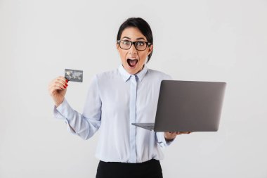 Beyaz arka plan üzerinde izole ofiste gümüş laptop ve kredi kartı tutan gözlük takıyor modern iş kadını portresi