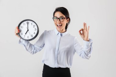 Mutlu heyecanlı işkadını akıllıca giyinmiş ayakta beyaz arka plan üzerinde izole çalar saat gösterilen