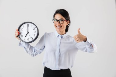 Mutlu heyecanlı işkadını akıllıca giyinmiş ayakta beyaz arka plan üzerinde izole çalar saat gösterilen