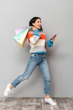 Esmer kadın koşma ile renkli 30s portresi alışveriş torbaları ve cep telefonu gri arka plan üzerinde izole el kağıt