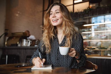 İçeride kahve içme not defterinde notlar yazma kafede oturan güzel genç güzel kadın fotoğrafı.