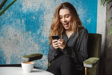 Kapalı cep telefonu sohbet kullanarak kafede oturan güzel genç güzel kadın fotoğrafı.