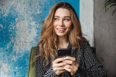 Kapalı cep telefonu sohbet kullanarak kafede oturan güzel genç güzel kadın fotoğrafı.