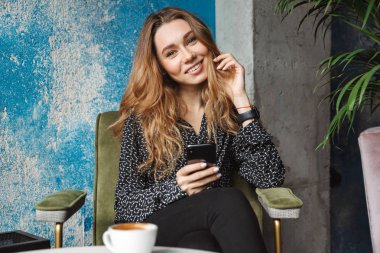 Kapalı cep telefonu sohbet kullanarak kafede oturan güzel genç güzel kadın fotoğrafı.