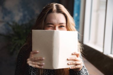 Güzel genç güzel kadın kapalı kapsayan yüz kitap okuma kafede oturan fotoğrafı.
