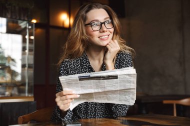 Görüntü güzel bir genç kadının kapalı gazete okuyan kafede oturan.