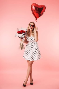 Buket gül ve kalp tutan pembe arka plan üzerinde izole ayakta elbise güzel genç sarışın bir kadın portresi tam uzunlukta balon şeklinde