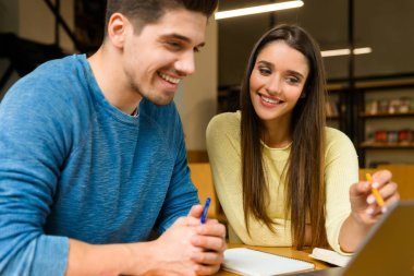 Fotoğraf kitaplığındaki okumak ev ödevi eğitim ve dizüstü bilgisayar kullanan bir iki genç öğrenci arkadaşlar çiftin.