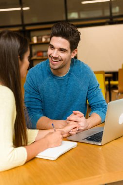 Genç öğrenciler arkadaş çift okumak ev ödevi eğitim ve dizüstü bilgisayar kullanan Kitaplığı'nda.